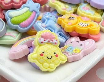 May include: Assortment of colorful, cartoon-themed resin embellishments, including a rainbow, a unicorn, a pineapple, a bunny, a shooting star, and a flower.
