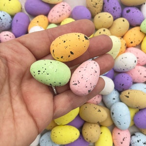 Può includere: Una collezione di uova di Pasqua macchiate di colori pastello. Le uova sono in varie tonalità di rosa, blu, verde, giallo e bianco. Alcune uova hanno un motivo macchiato, mentre altre hanno un colore solido.