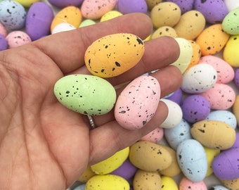 May include: A collection of pastel colored speckled Easter eggs. The eggs are in various shades of pink, blue, green, yellow, and white. Some of the eggs have a speckled pattern, while others have a solid color.
