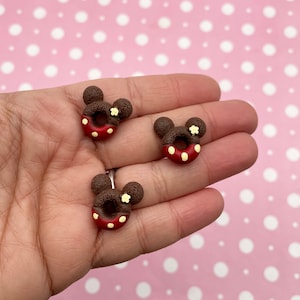 May include: Three brown and red donut shaped charms with Mickey Mouse ears and white flower accents.