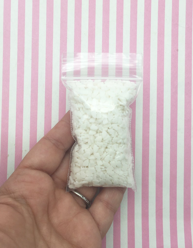 May include: A clear plastic bag filled with small, white, irregularly shaped pieces. The bag is held against a pink and white striped background. The bag is sealed with a zipper closure.