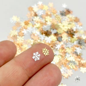 A hand holding two small snowflake-shaped objects against a background of scattered golden and white snowflake-shaped objects.