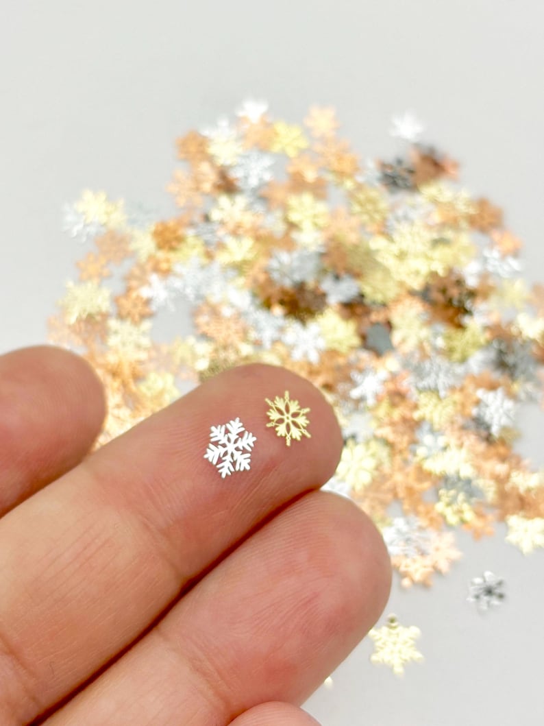 A hand holding two small snowflake-shaped objects against a background of scattered golden and white snowflake-shaped objects.