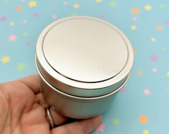 May include: A silver metal tin with a lid. The tin is round and has a smooth surface.