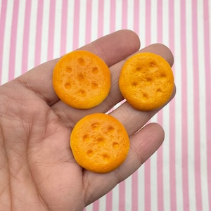 May include: Three small, round, yellow crackers with a textured surface and small holes.