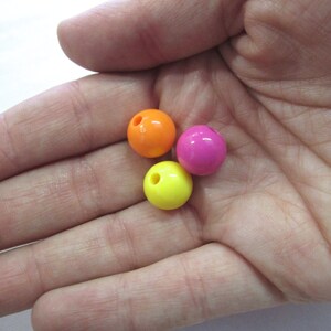 May include: Three round plastic beads in bright colours: orange, pink, and yellow. The beads have a hole in the centre for stringing.