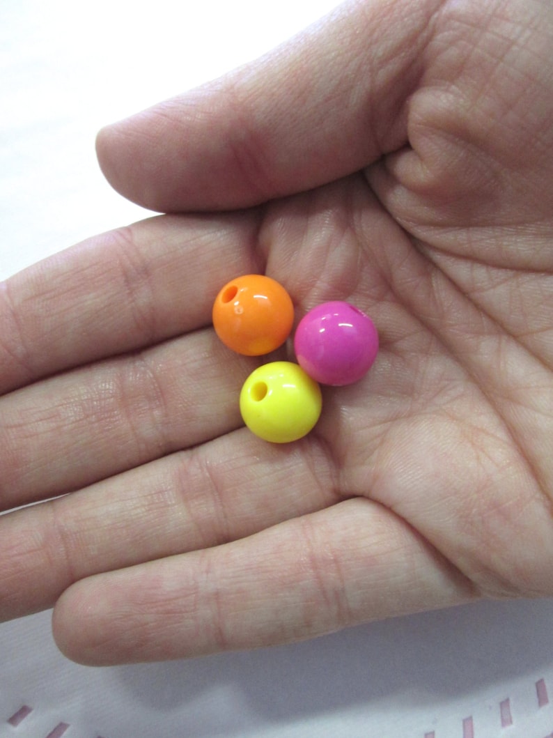 May include: Three round plastic beads in bright colours: orange, pink, and yellow. The beads have a hole in the centre for stringing.