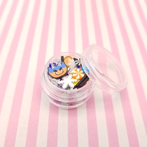 Peut inclure: Un r&eacute;cipient en plastique transparent rempli de charmes en plastique color&eacute;s et blancs, dont un personnage bleu et orange avec un nez rouge, des flocons de neige et des cannes en sucre. Le r&eacute;cipient a un couvercle transparent.