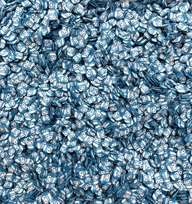 K&ouml;nnte beinhalten: Ein gro&szlig;er Haufen blauer und wei&szlig;er Milchpackungsstreusel. Die Packungen haben ein s&uuml;&szlig;es Comic-Gesicht mit einem L&auml;cheln und Augen.
