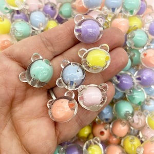 May include: A collection of pastel-colored bear-shaped beads. The beads are made of clear plastic with a colored bear inside. The beads are in various colors, including pink, blue, yellow, and green.