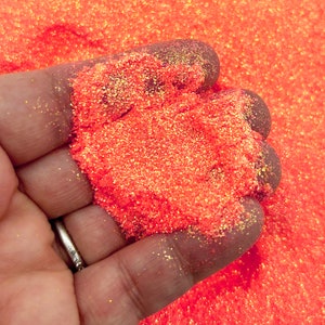 Op de afbeelding: Een close-up van een hand die een hoop feloranje glitter met een gouden schittering vasthoudt.