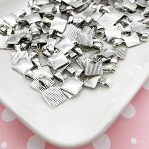 May include: A pile of silver-toned metal square pendant bails with a textured surface. The bails have a loop at the top for attaching a chain or cord.