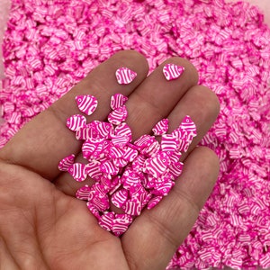 May include: A close-up of a hand holding a pile of pink and white fish-shaped sprinkles. The sprinkles are small and have a white outline.