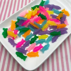 May include: A white plate filled with colorful gummy fish shaped candies. The candies are in various shades of pink, purple, blue, green, yellow, and orange.