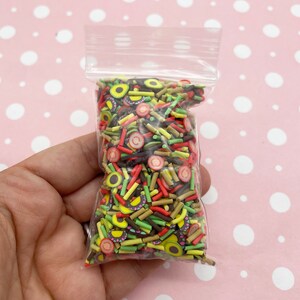 May include: A clear plastic bag filled with colorful sprinkles. The sprinkles are shaped like avocado slices, strawberries, and brown sticks.