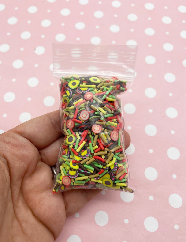 May include: A clear plastic bag filled with colorful sprinkles. The sprinkles are shaped like avocado slices, strawberries, and brown sticks.
