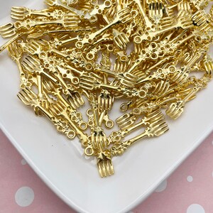 May include: A pile of gold-colored metal fork charms with decorative details. The charms have a loop at the top for attaching to jewelry or other crafts.