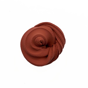 May include: A top-down view of a swirl of terracotta-colored material against a white background. The material has a textured, slightly granular appearance, with visible ridges and folds. The shape resembles a tightly wound spiral or a rose.