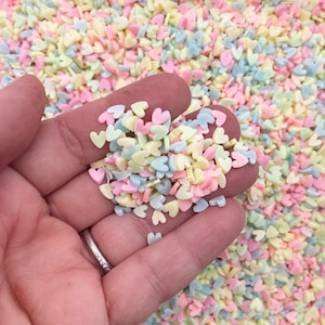 May include: A handful of pastel pink, yellow, and blue heart-shaped sprinkles.