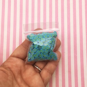 May include: A small clear plastic bag filled with blue and green round sprinkles. The sprinkles have a green and white pattern.
