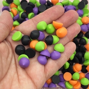 以下が含まれることがあります： 黒、緑、オレンジ、紫の小さなカラフルなプラスチック製の尖った形が詰め合わせられています。形は手に持たれており、背景にはさらに多くの形があります。