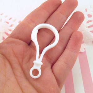 May include: White plastic key chain loop with a round opening. The loop is held in a hand.