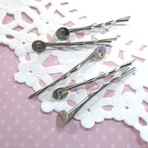 May include: Five silver bobby pins with a decorative round end. The bobby pins are twisted and have a silver finish.