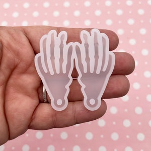May include: Two white silicone moulds shaped like skeleton hands. The moulds are designed for making resin crafts.