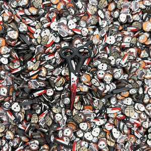 May include: A close-up image of a large pile of Halloween-themed resin charms. The charms are in the shape of various horror movie characters, including a clown, a masked killer, and a bloody knife. There is a pair of black scissors with a red handle in the center of the image.