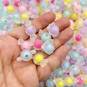 May include: A collection of pastel-colored candy-shaped beads with clear plastic wrappers. The beads are in a variety of colors, including pink, blue, yellow, and purple.