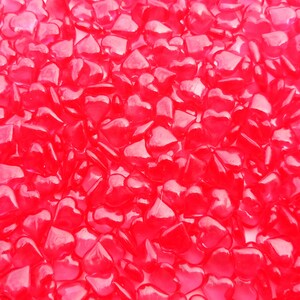 May include: A close-up image of a large quantity of small, bright red heart-shaped glass beads.