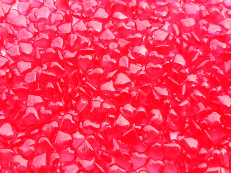 May include: A close-up image of a large quantity of small, bright red heart-shaped glass beads.