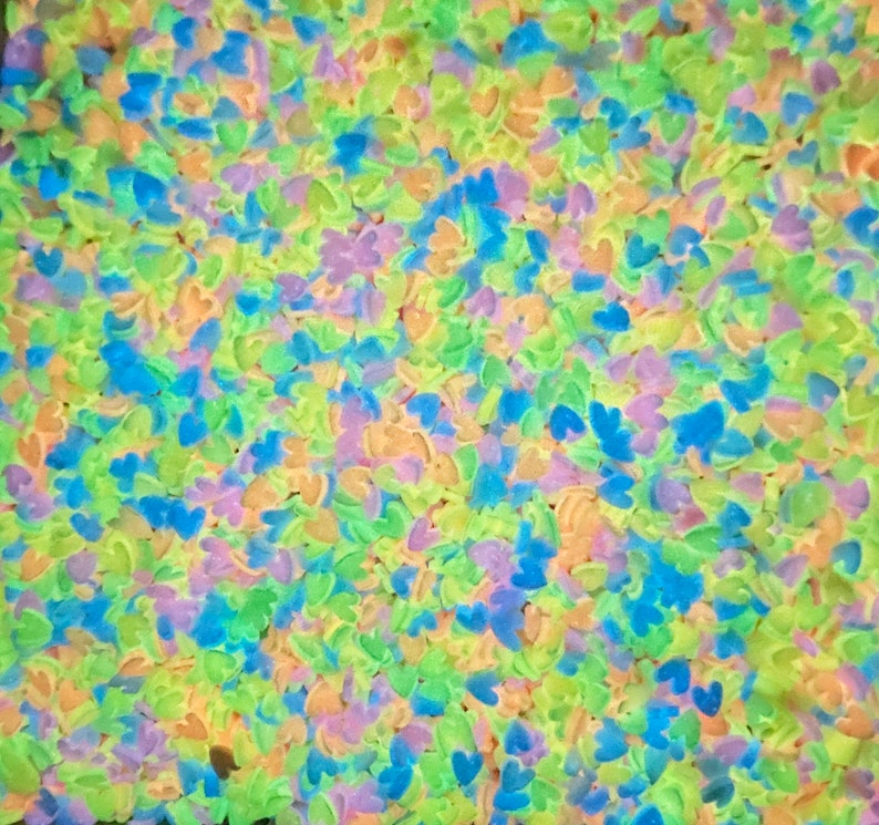 May include: A close-up image of a large quantity of small, heart-shaped sprinkles in a variety of pastel colors, including blue, green, yellow, and purple.