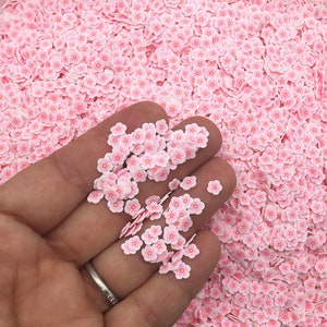 Puede incluir: Primer plano de una mano sosteniendo un montón de pequeñas chispas rosas en forma de flor. Las chispas están esparcidas sobre una superficie.