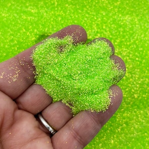 May include: A close-up of a hand holding a pile of bright green glitter. The glitter is fine and has a slight iridescent sheen.