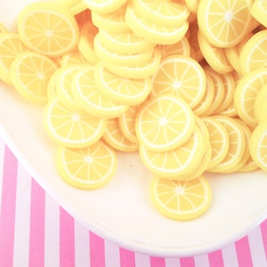 May include: A white plate filled with yellow lemon slices. The plate is on a pink and white striped surface.