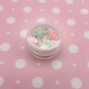 May include: A small clear jar filled with pastel-colored heart and star-shaped sprinkles.