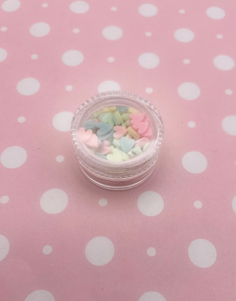 May include: A small clear jar filled with pastel-colored heart and star-shaped sprinkles.