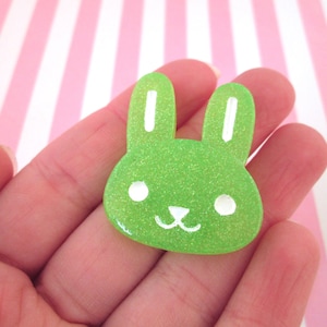 May include: A green glitter bunny rabbit charm with white ears and eyes. The charm is made of resin and has a glossy finish.