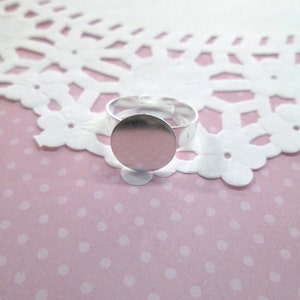 May include: A silver ring with a round, blank, silver bezel. The ring is on a pink background with white polka dots.