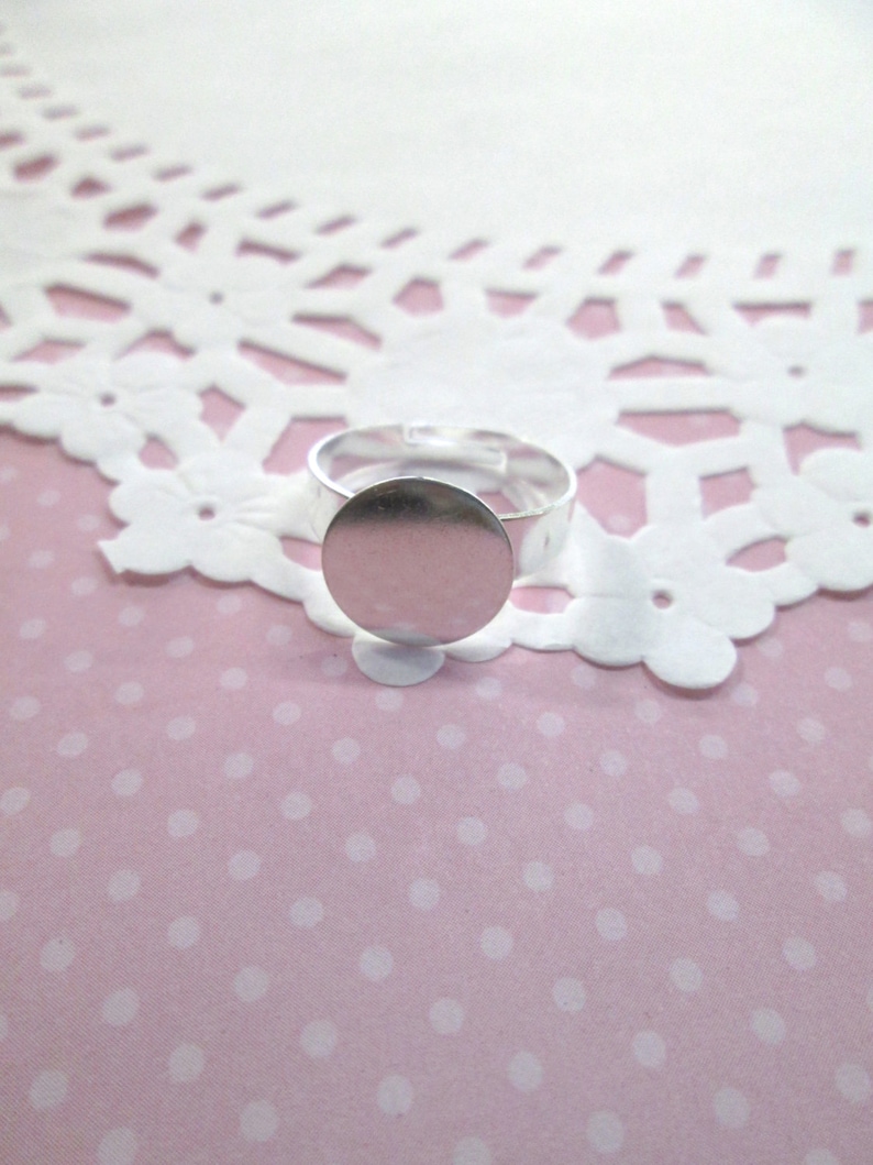 May include: A silver ring with a round, blank, silver bezel. The ring is on a pink background with white polka dots.