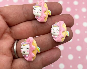 May include: Three pink and yellow donut charms with a white unicorn peeking out of each donut. The unicorn has a rainbow horn and tail.
