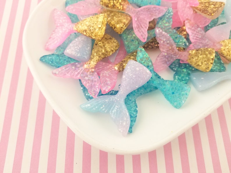 Puede incluir: Un mont&oacute;n de abalorios de cola de sirena con purpurina de colores rosa, azul y dorado. Los abalorios est&aacute;n hechos de resina y tienen un acabado brillante.