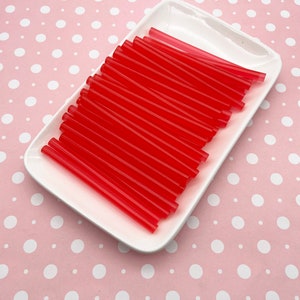 May include: A white ceramic plate filled with a stack of red plastic drinking straws.