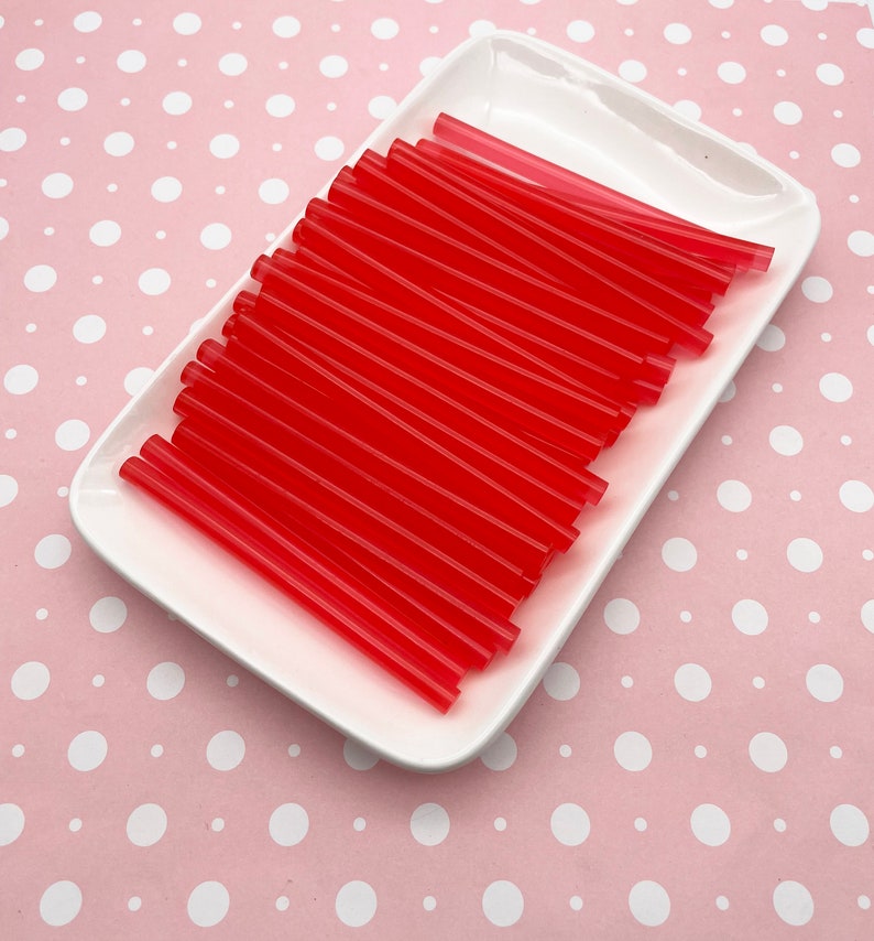May include: A white ceramic plate filled with a stack of red plastic drinking straws.