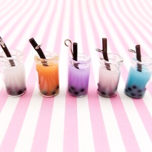 Pu&ograve; includere: Cinque vasetti di vetro in miniatura con cannucce nere e bubble tea colorato all'interno. I vasetti sono disposti in fila su una superficie a righe rosa e bianche.