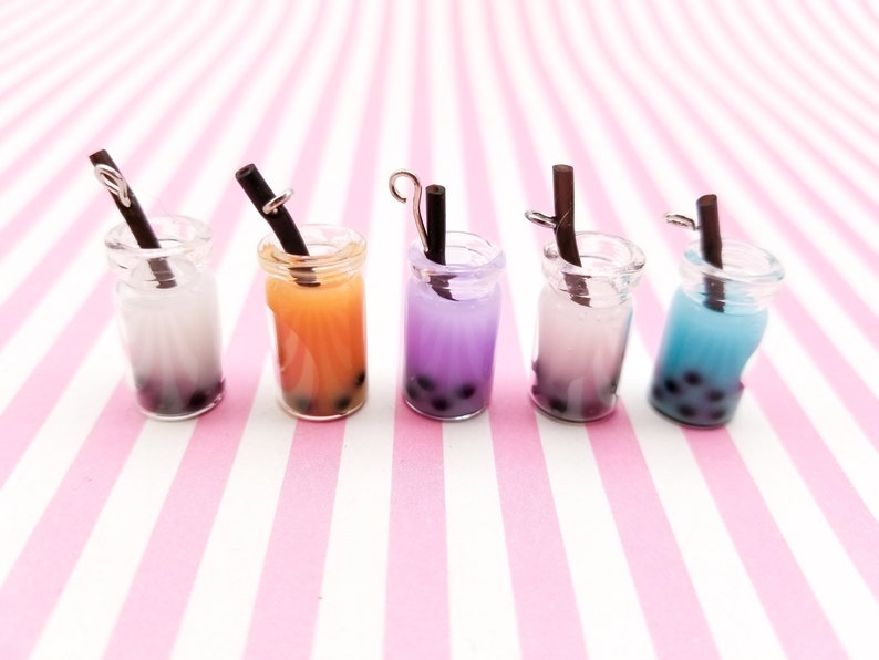 Pu&ograve; includere: Cinque vasetti di vetro in miniatura con cannucce nere e bubble tea colorato all'interno. I vasetti sono disposti in fila su una superficie a righe rosa e bianche.