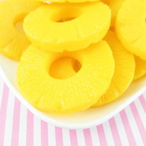 May include: A white plate with yellow pineapple rings on a pink and white striped surface.