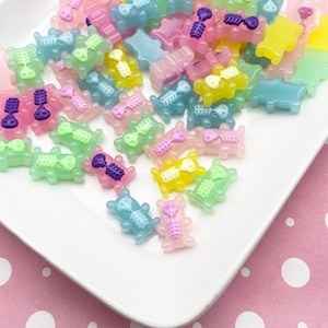 Può includere: Una collezione di ciondoli colorati e traslucidi a forma di orsetto con disegni di scheletri interni. I ciondoli sono in vari colori pastello, tra cui rosa, blu, verde e giallo, e sono disposti su un piatto bianco.