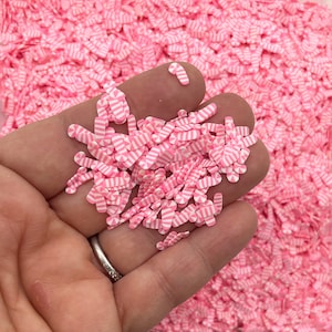 May include: A close-up of a hand holding a pile of pink and white candy cane sprinkles. The sprinkles are small and have a candy cane design.